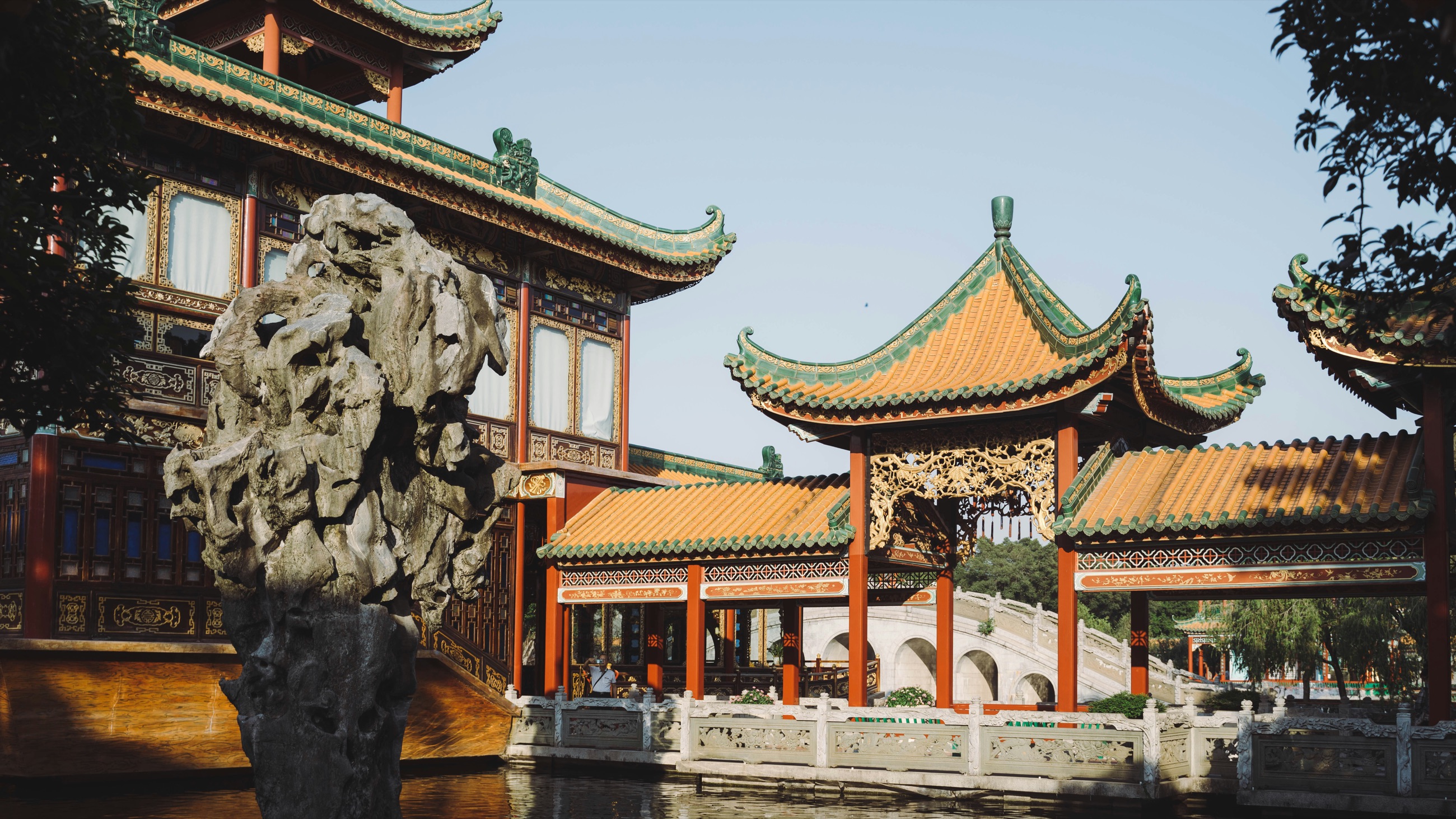 Pavilions with green-glazed roofs and vermilion columns beside a garden rock and water